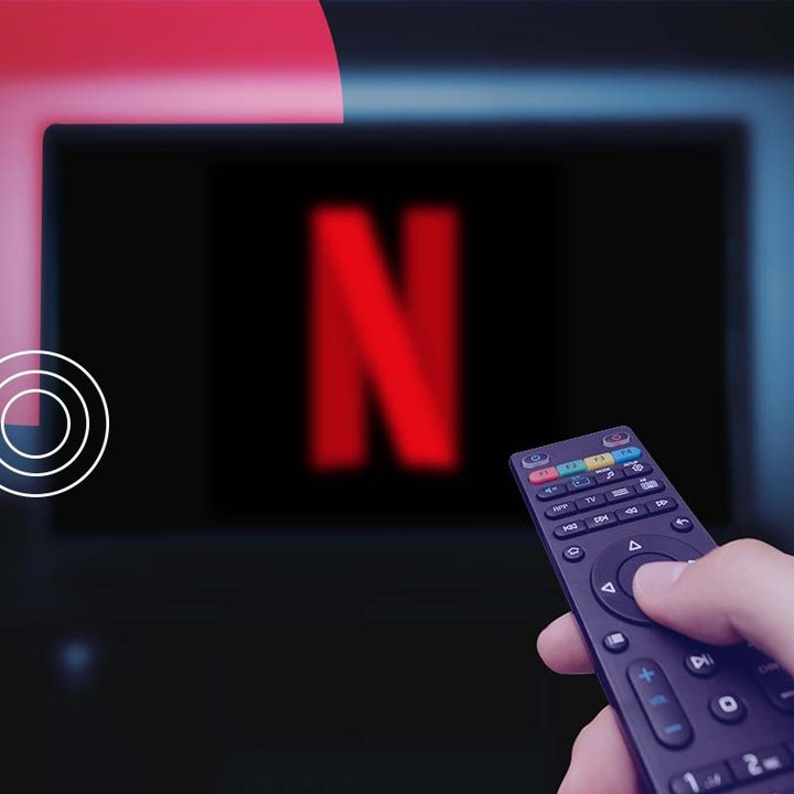Una mano sosteniendo un control remoto y apuntando hacia el televisor con Netflix.