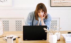 Una mujer con expresión frustrada observa una laptop en un escritorio.