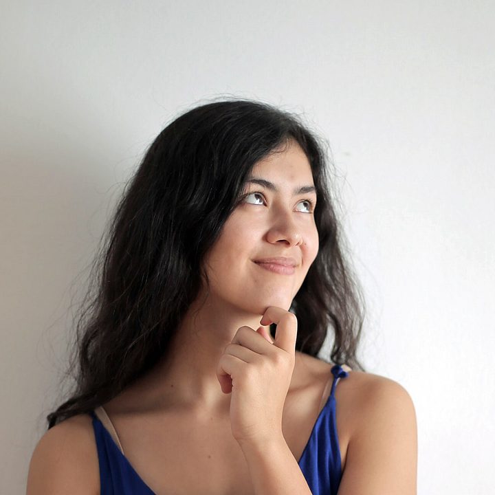 Una mujer parada frente a un fondo blanco con gesto de interrogaci&oacute;n sonriente.