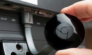 Persona sostiene un dispositivo Chromecast conectado a un televisor – Cómo conectar Chromecast en el televisor de la habitación de un hotel.