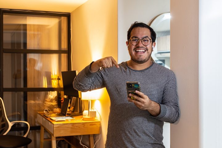 Latino feliz con su teléfono celular en la mano.