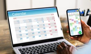 Persona con un calendario digital abierto en su computador y en su teléfono celular – Encuentra aquí la mejor app de calendario para iOS y Android.