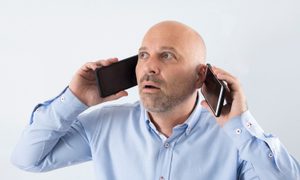 HOMBRE CON UN CELULAR EN CADA OREJA Y CARA DE CONFUSUIÓN – Las mejores apps para tener un segundo número de teléfono.