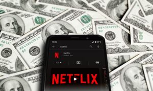 Celular con app. de Netflix sobre billetes de 100 dólares – ¿Cuánto cuesta Netflix? Te explicamos todos sus planes y sus precios.