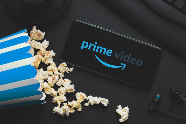 Paquete volteado de popcorn junto con un celular con el logo de Prime Video en su pantalla – Cómo descargar películas de Amazon Prime Video.