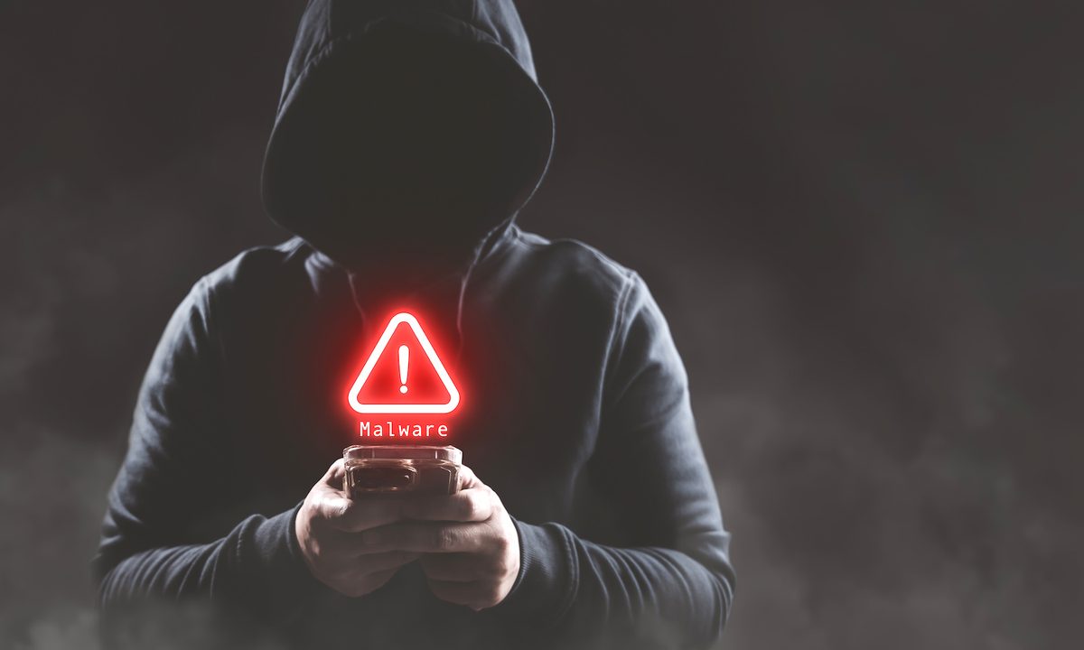Persona con una capucha y un celular con la señal de Alert – Cómo eliminar un virus en tu dispositivo Android.