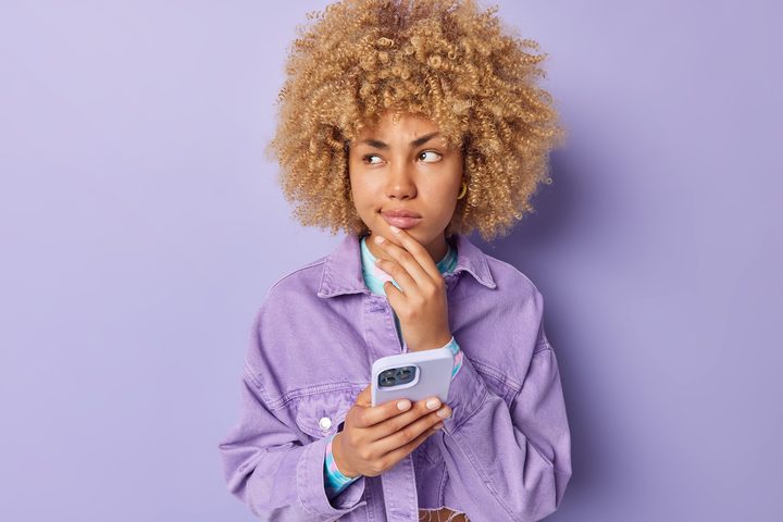 Chica joven y pensativa con un celular en la mano – El ojo público todo lo ve, y esto es un aspecto que define a las redes sociales. No tienes que ser un actor o un músico famoso: tu vida queda expuesta al resto del mundo cada vez que publicas una foto en Instagram.