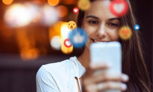 Mujer joven riendo mientras revisa sus redes sociales en un celular – Cómo vincular Instagram con Facebook.