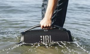 Una persona sosteniendo el parlante JBL Boombox 3 sobre el mar.