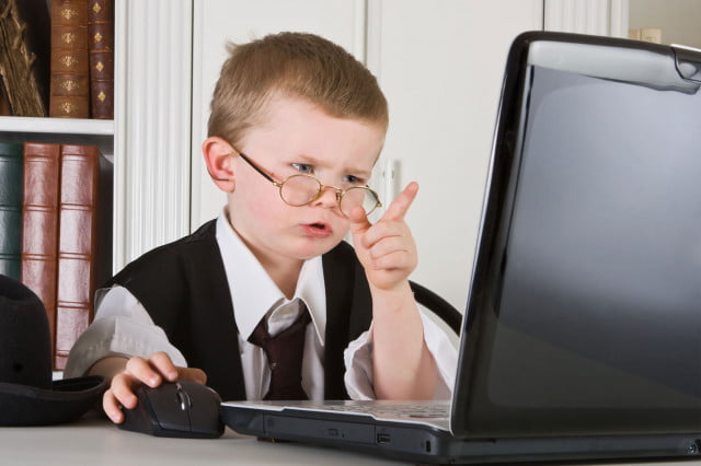 Un niño con lentes vestido con traje como adulto frente a una computadora con controles parentales