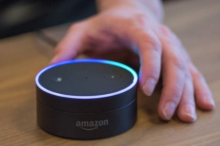 Una mano acomodando un asistente virtual de Amazon sobre una superficie para aprender cómo conectar Alexa al TV