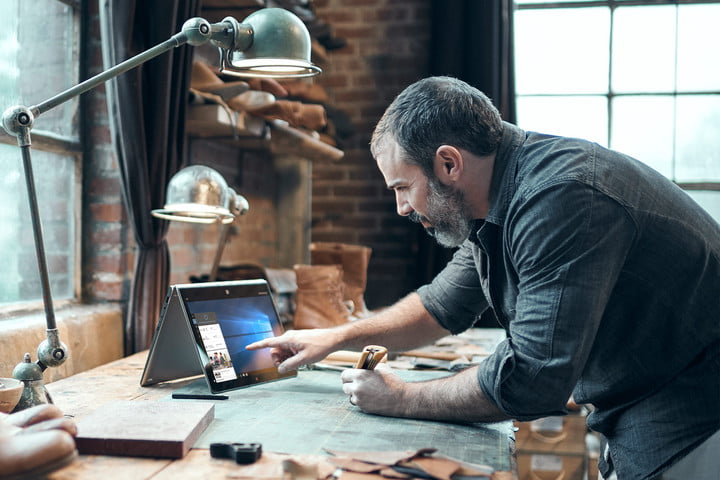 Un hombre selecciona su computadora portátil mientras trabaja apoyado en su escritorio 