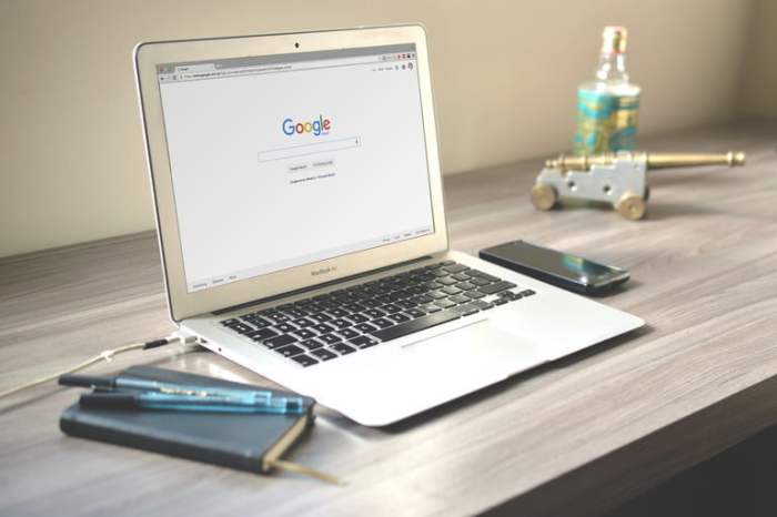 establecer Google como página de inicio .una laptop abierta con el buscador de googlle y un teléfono y una agenda a los lados