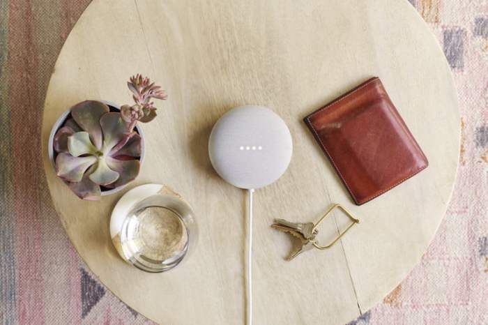 Google Nest Mini blanco sobre una mesa junto con otros objetos, un vaso, una cartera, unas llaves y una planta