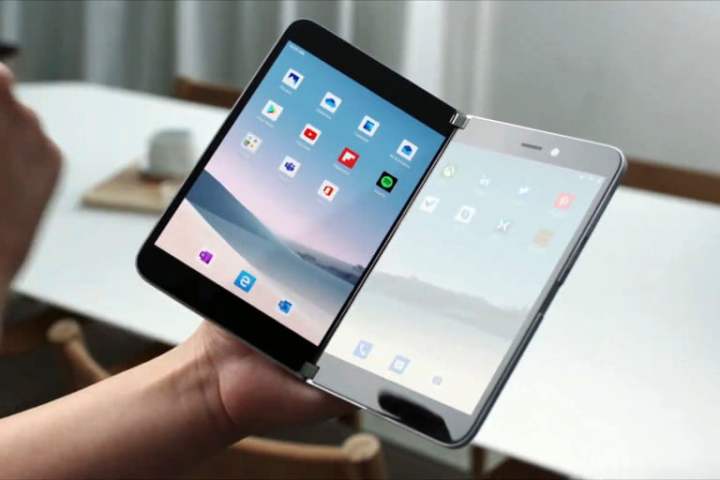 Surface Duo abierta en la mano de una persona y con imagen en pantalla del escritorio con iconos