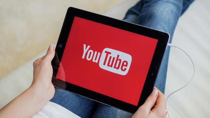 Una persona sostiene una tableta iPad con el logo de Youtube. para aprender Cómo subir un video a YouTube