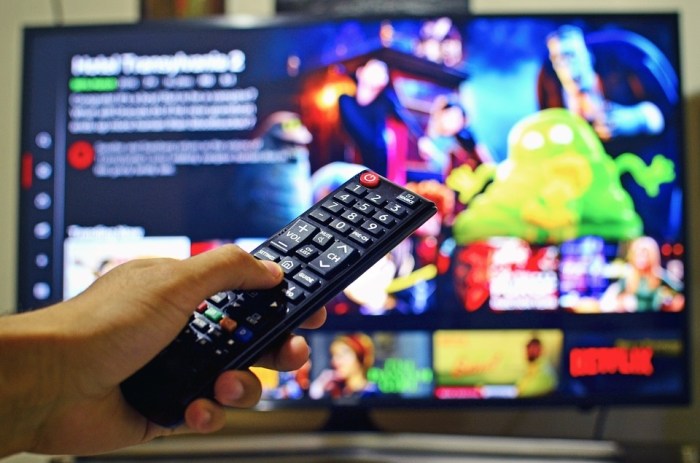 Una persona apunta el control remoto hacia un televisor en el que se proyecta el menú de Netflix