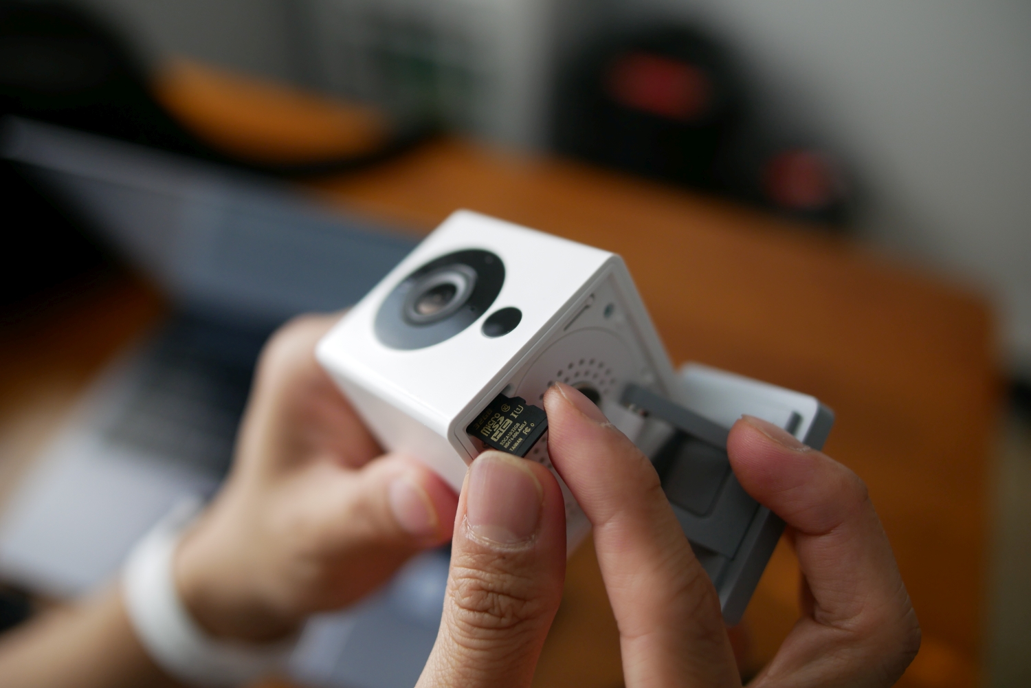 Wyze Cam en las manos de una persona, insertando una microSD card para actualizar el firmware