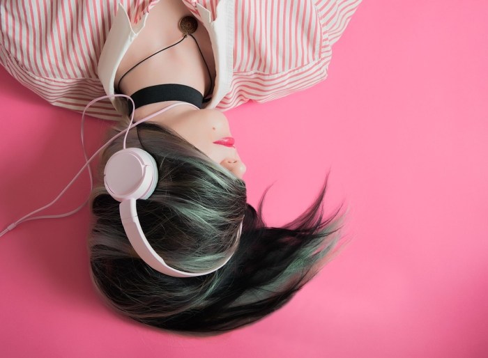 Una mujer con audífonos sobre un fondo de color rosa