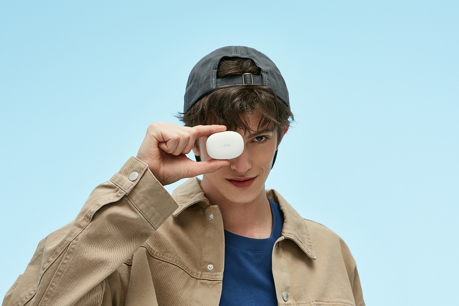 Un joven sujeta entre sus dedos el estuche cargador de los auriculares Realme Buds Q de color blanco