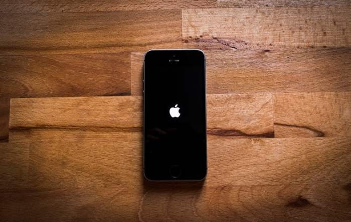 Celular sobre superficie de madera reiniciándose para revisar qué hacer cuando tu iPhone no carga la batería