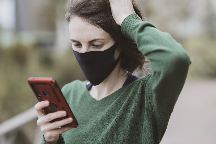 Una mujer usa una mascarilla mientras revisa su teléfono celular