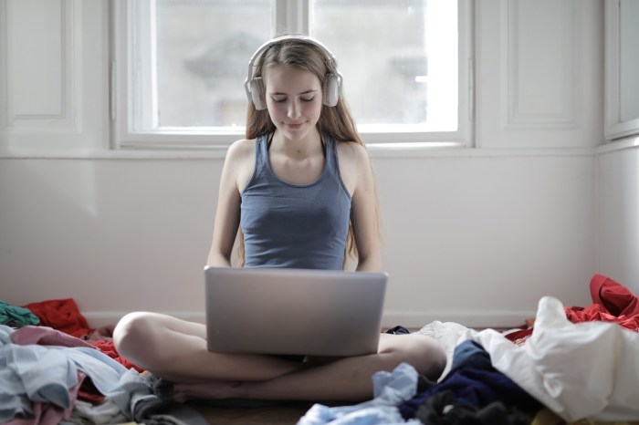 joven con unos auriculares de diadema usando un portátil sentada en el suelo