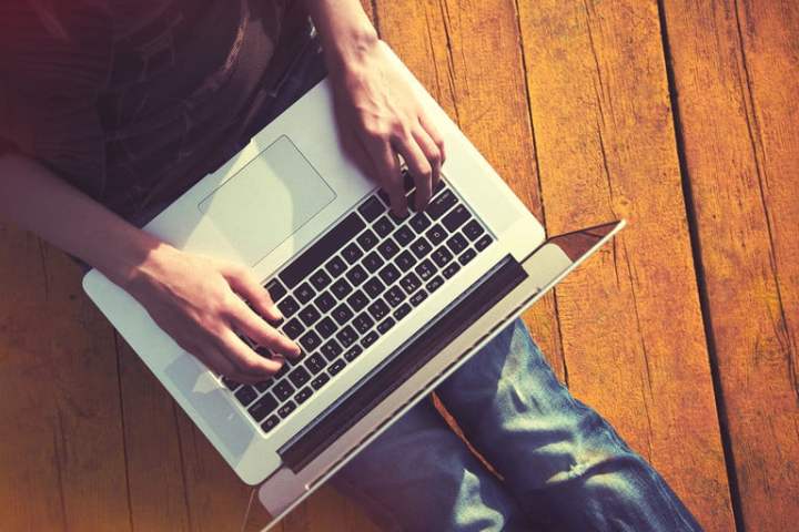 Una persona sentada en el suelo con una laptop sobre sus piernas para aprender cómo resetear PRAM y SMC