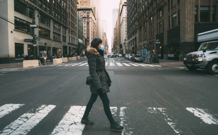 La imagen muestra a una mujer con mascarilla caminando en una ciudad casi vacía.
