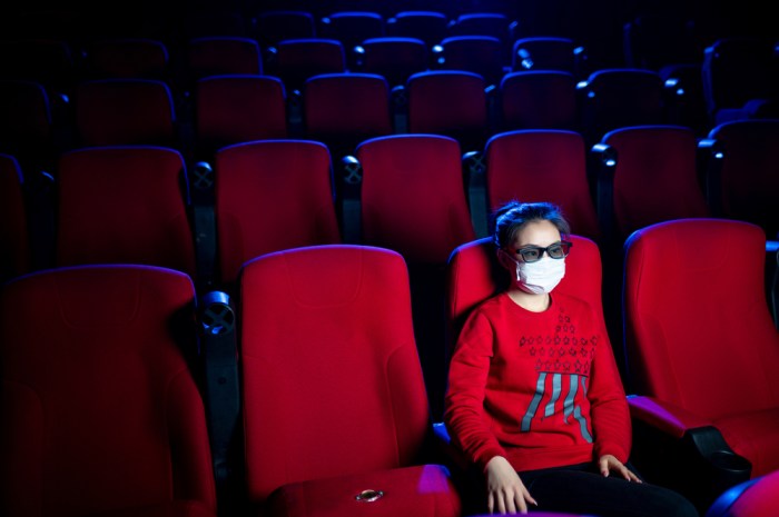 La imagen muestra a una mujer conmascarilla sentada sola en una sala de cine.