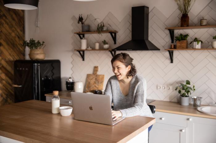 Una mujer ríe mientras usa una MacBook en su cocina.