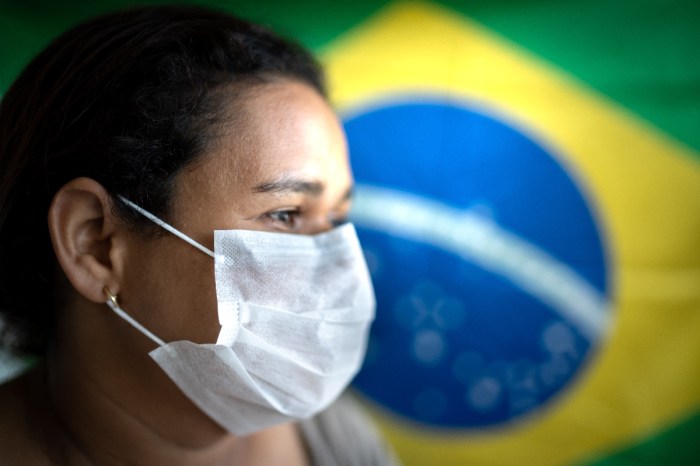 Una mujer usa una mascarilla con la bandera brasileña de fondo