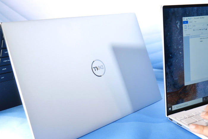 Dos laptop Dell, una abierta y encendida y otra en modo tienda, sobre una superficie azul, para comparar la Dell XPS 13 vs. MacB