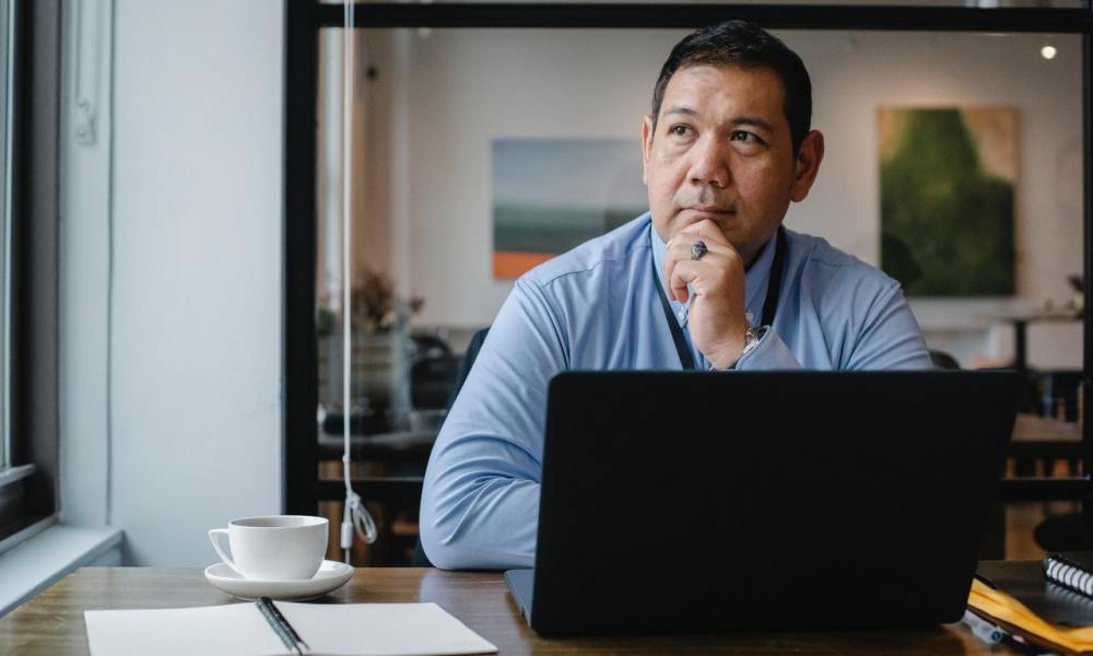 Un hombre reflexiona mientras trabaja en una laptop en una oficina.