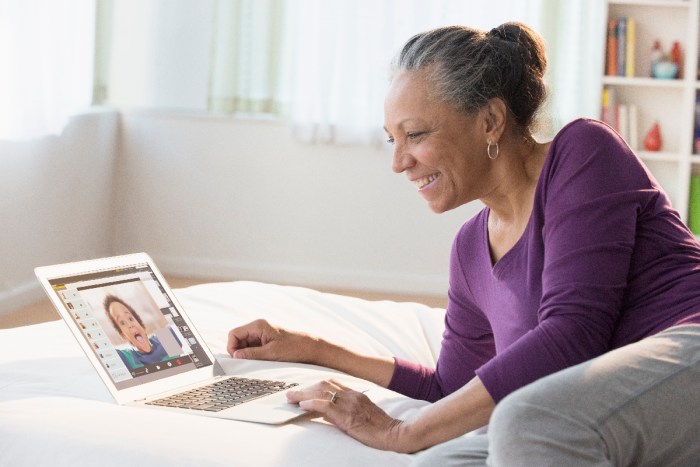 Una mujer adulta usa una computadora para mantener una videoconferencia con su nieto.