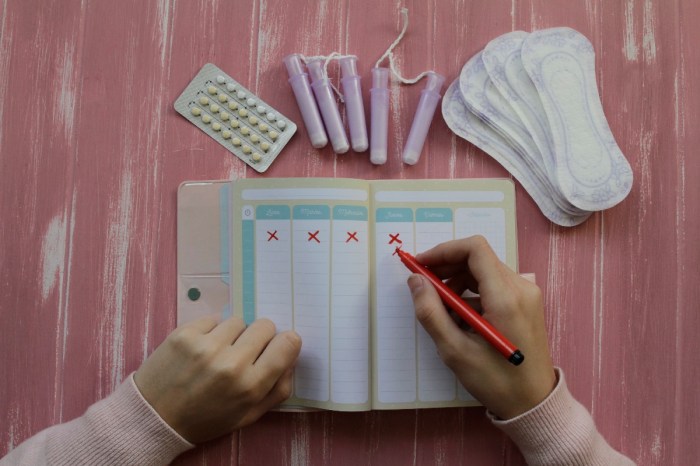Una mujer anota en una agenda su ciclo menstrual sobre un escritorio, donde además hay tampones, protectores y píldoras anticonceptivas