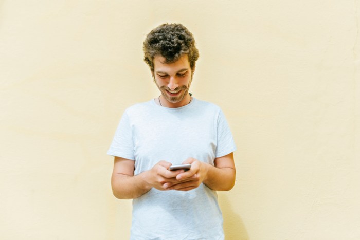 cinco aplicaciones utiles para escritores incipientes man using mobile phone with yellow wall background