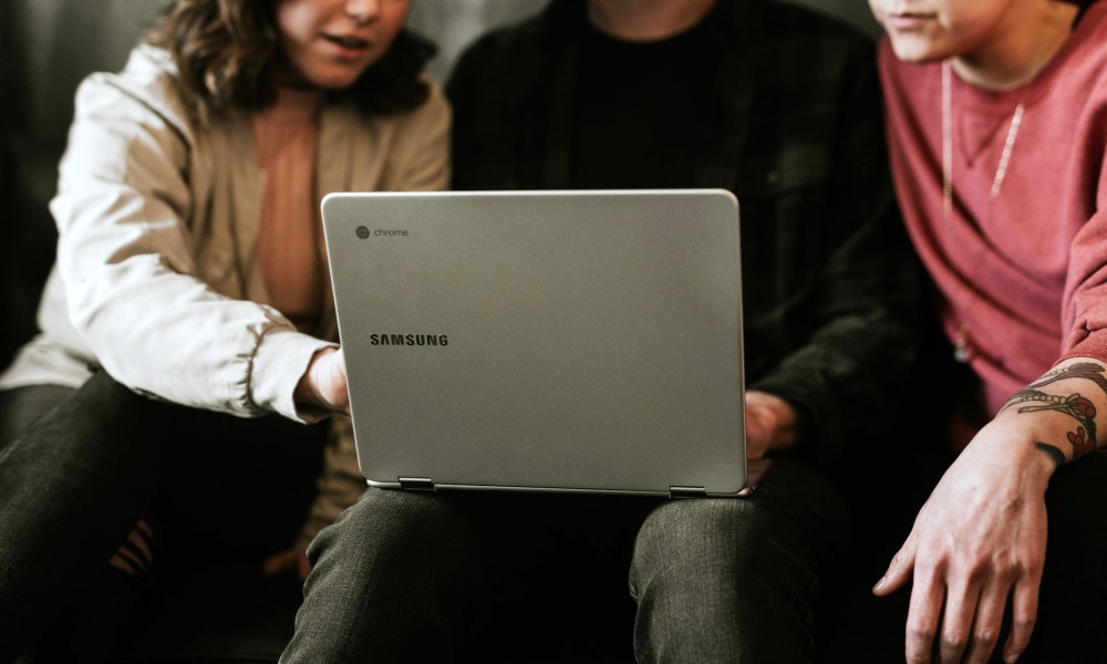 Una mujer explicándole a un hombre con una laptop en sus piernas cómo hacer una captura de pantalla en una Chromebook.