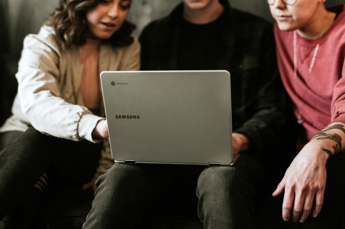 Una mujer explicándole a un hombre con una laptop en sus piernas cómo hacer una captura de pantalla en una Chromebook.