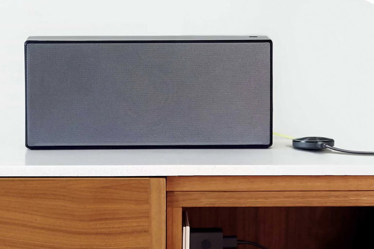 Google Chromecast en color negro sobre un escritorio junto a un altavoz