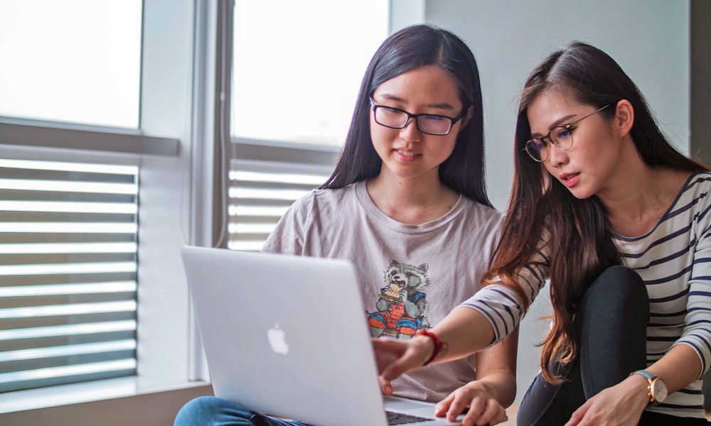 dos chicas con una macbook aprenden cómo descargar videos de facebook