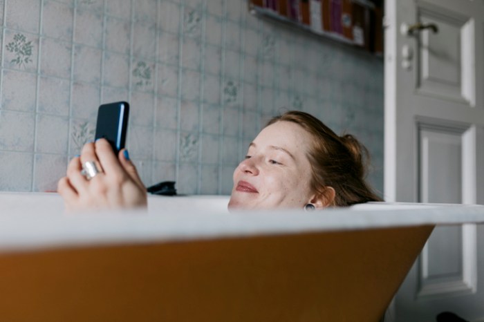 La imagen muestra a una mujer en la bañera mirando su teléfono celular.
