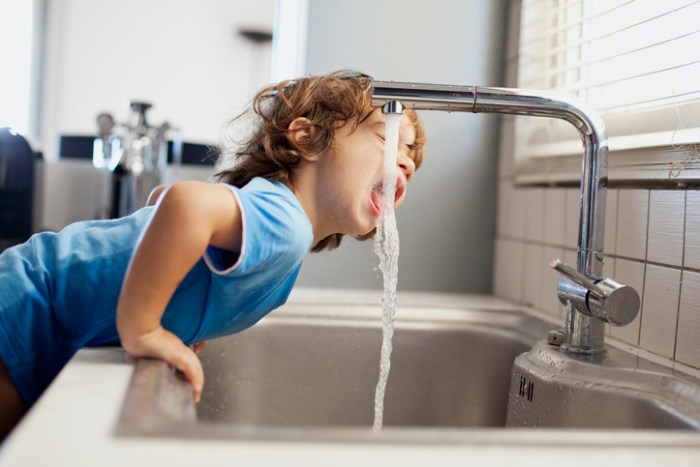 La imagen muestra a un niño tomando agua desde la llave.