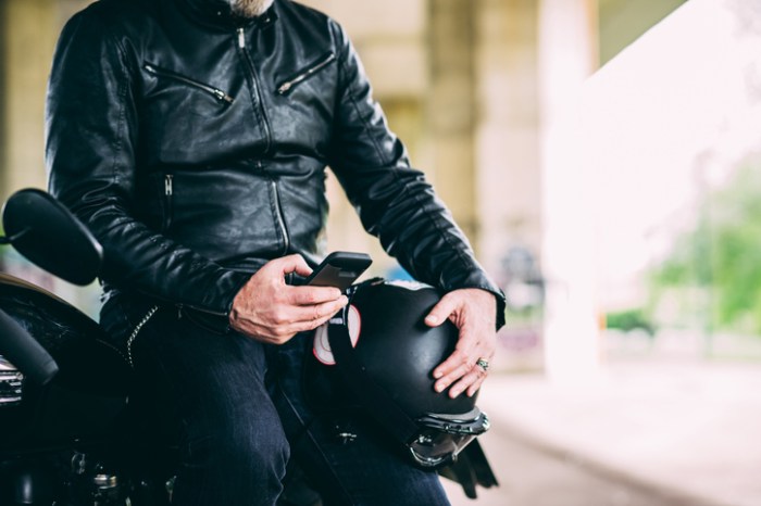 La imagen muestra a un motociclista revisando su teléfono celular.