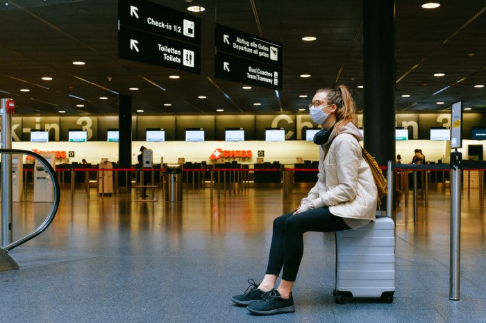 Mujer sentada sobre una maleta en lo que parece ser un aeropuerto.
