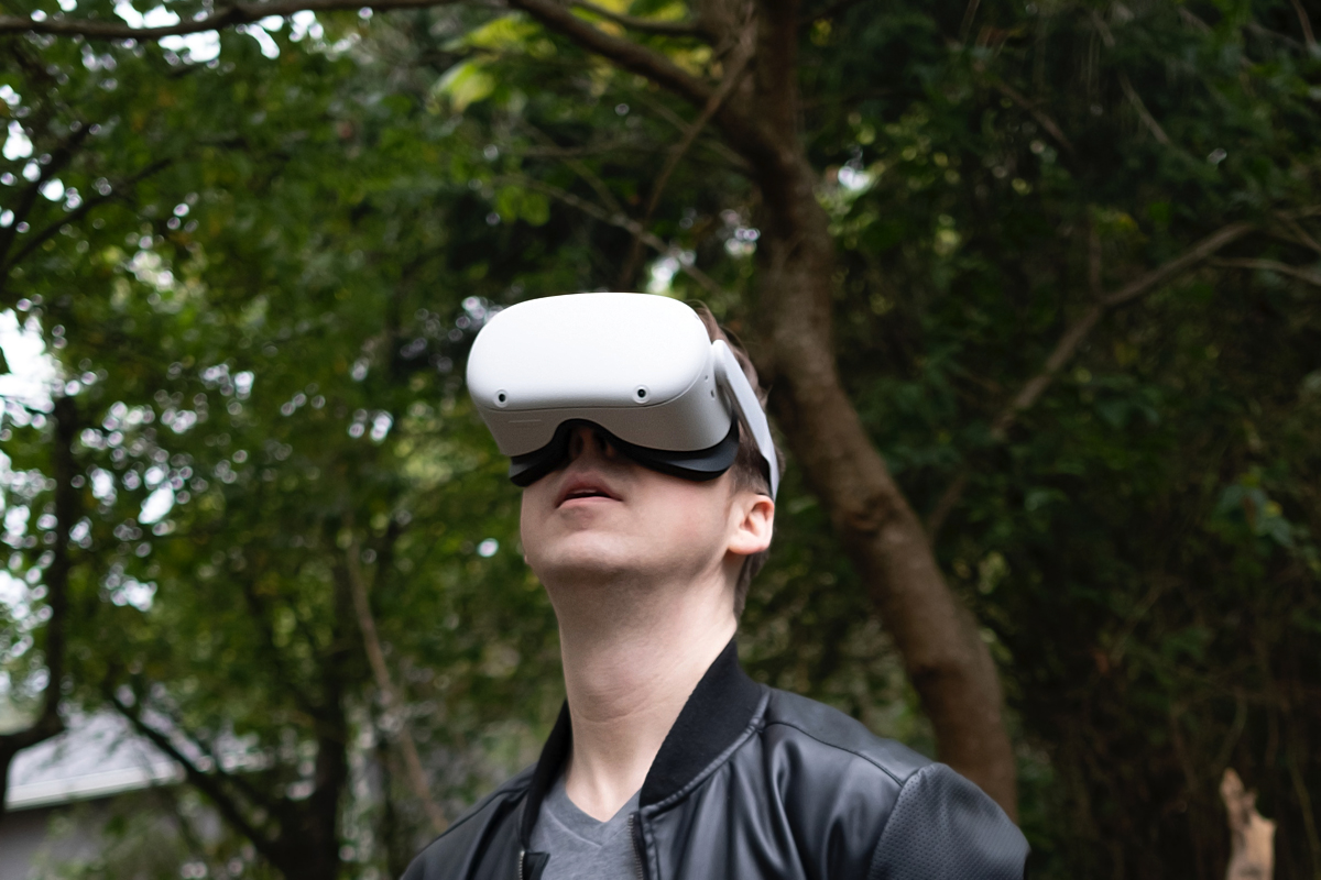 Un hombre con un visor de realidad virtual mira hacia arriba entre árboles.