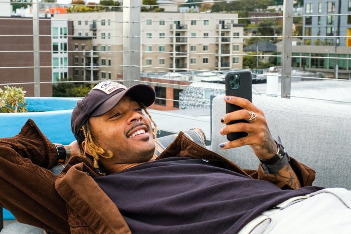 Un hombre, recostado en un balcón, sonríe mientras utliza su celular para enviar mensajes.