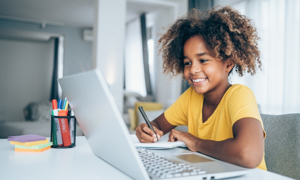 Una niña está sentada frente a una computadora en clases remotas.