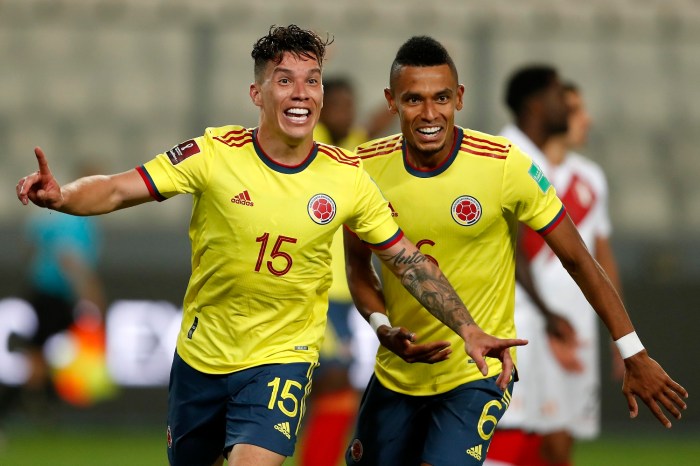 Mateus Uribe de la selección de fútbol de Colombia corre a través del campo para celebrar un gol, mientras es perseguido por su compañero de equipo William Tesillo.