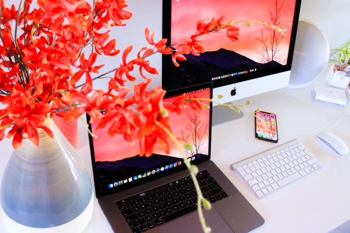 Un Macbook, un iMac , un iPhone y un teclado inalámbrico de Apple junto a un florero de colores vivos.
